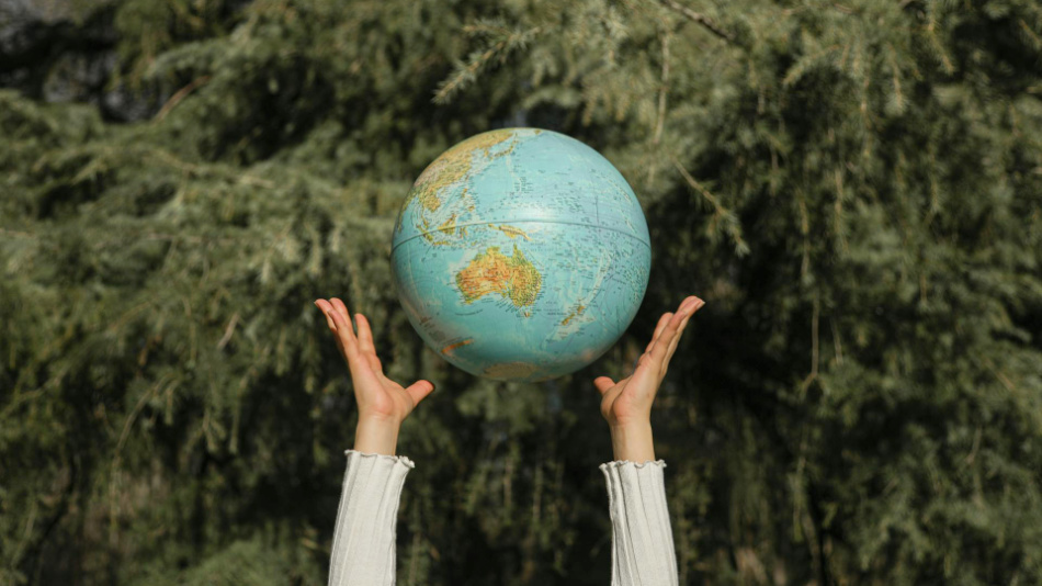 Natur i bakgrunden och två händer som kastar en glob i luften för att symbolisera harmoni med naturen och miljön.