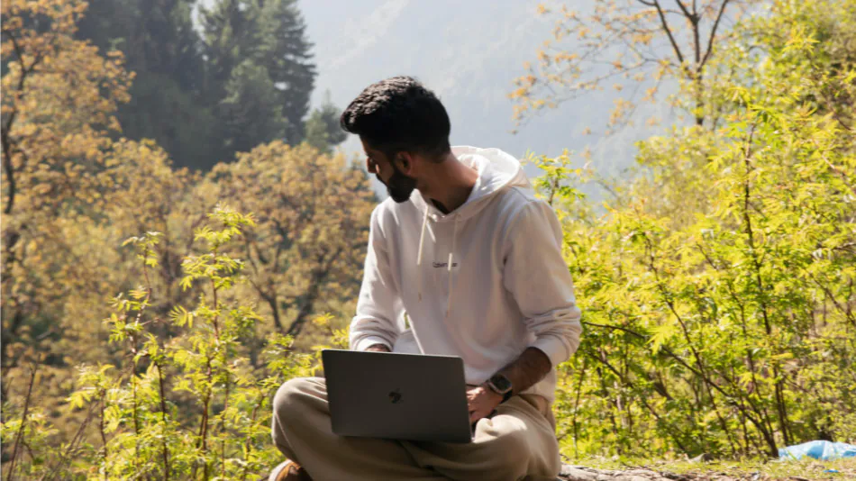 En ung man som sitter i naturen med sin laptop.